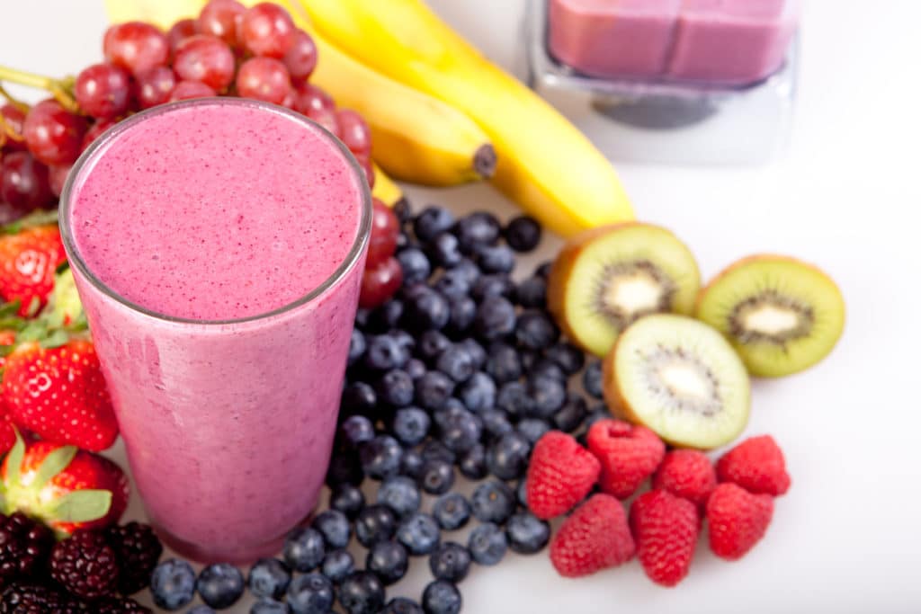 Pink smoothie in a glass surrounded by brightly colored fruit.