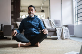 Man meditates on his floor at home.