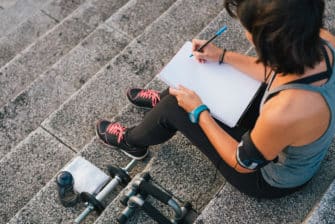 Woman writes down her fitness goals, while sitting on steps, before she begins her workout.