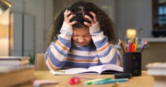 A young student holds her head and looks frustrated due to school stress.