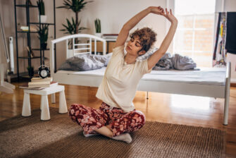 Woman does yoga routine next to her bed as part of her morning routine.