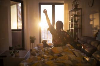 A woman sits on her bed and stretches after a good night's rest and a sleep cycle that is positively impacted by her nutrition.